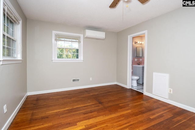 unfurnished bedroom with connected bathroom, an AC wall unit, ceiling fan, and dark wood-type flooring