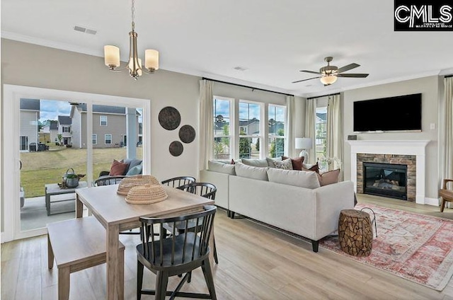 dining room with crown molding, a fireplace, light hardwood / wood-style floors, and ceiling fan with notable chandelier