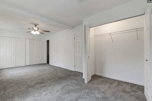 unfurnished bedroom featuring ceiling fan, dark carpet, a textured ceiling, and multiple closets