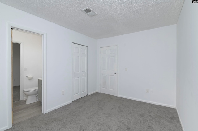 unfurnished bedroom with a textured ceiling, light colored carpet, and connected bathroom