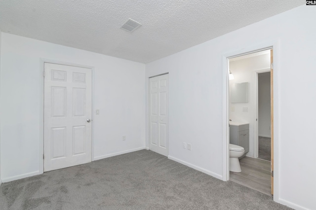 unfurnished bedroom with light colored carpet, a textured ceiling, and connected bathroom