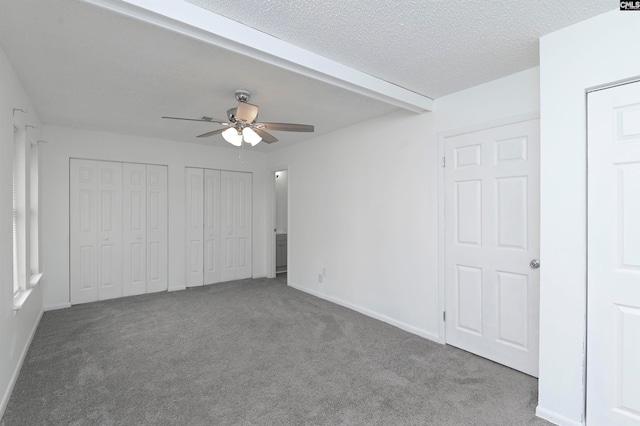 unfurnished bedroom with a textured ceiling, carpet floors, two closets, and ceiling fan