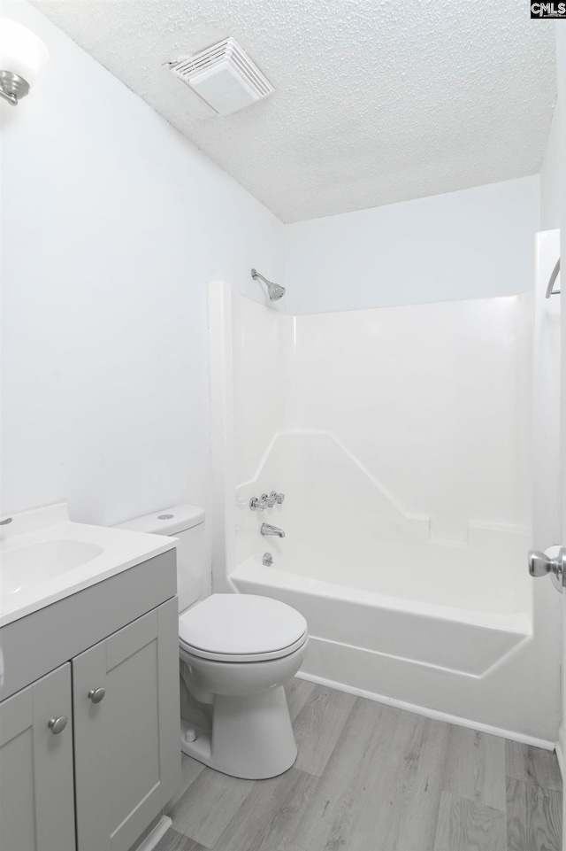 full bathroom with vanity, washtub / shower combination, toilet, a textured ceiling, and wood-type flooring