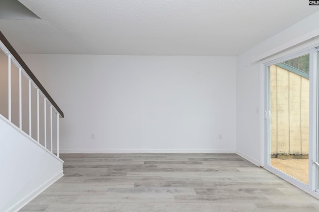 empty room with light wood-type flooring and a textured ceiling