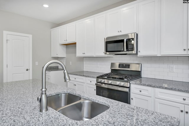 kitchen with backsplash, light stone counters, stainless steel appliances, sink, and white cabinets