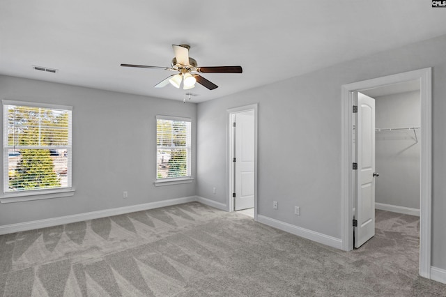 unfurnished bedroom featuring a closet, a walk in closet, light colored carpet, and ceiling fan