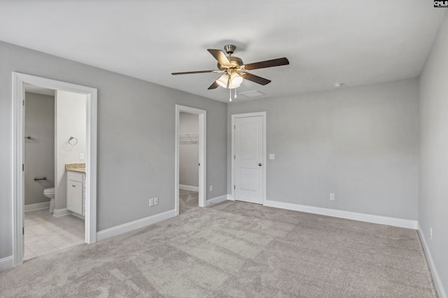 unfurnished bedroom featuring light carpet, ceiling fan, a spacious closet, connected bathroom, and a closet