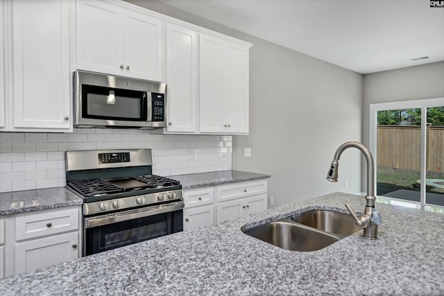 kitchen with light stone countertops, backsplash, stainless steel appliances, sink, and white cabinets