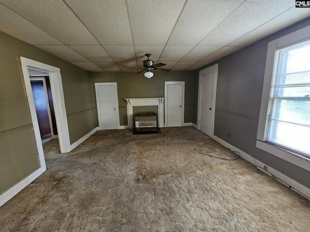 unfurnished living room featuring a paneled ceiling, ceiling fan, carpet, and a healthy amount of sunlight