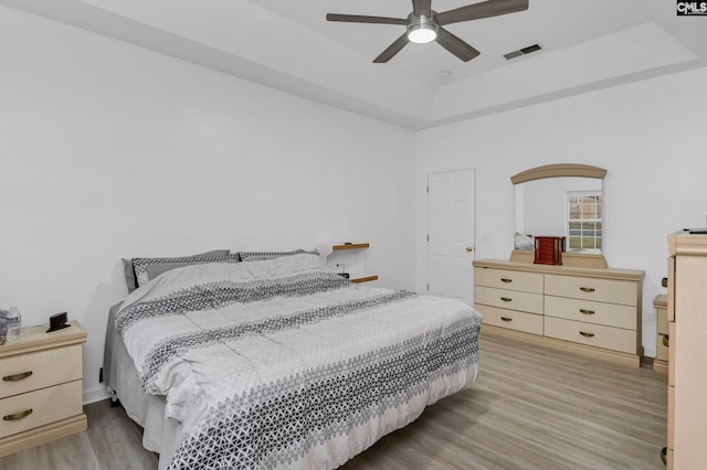 bedroom with hardwood / wood-style floors, ceiling fan, and a tray ceiling