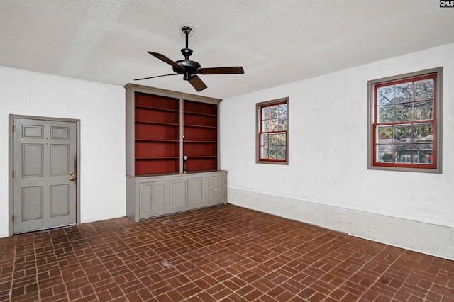 empty room with plenty of natural light, ceiling fan, a textured ceiling, and built in shelves