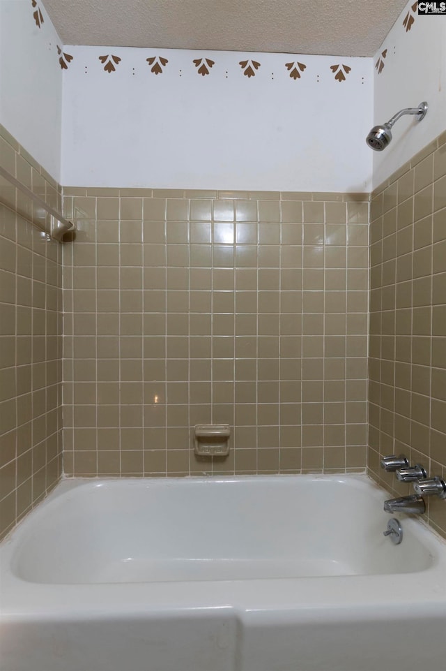 bathroom featuring a textured ceiling and tiled shower / bath