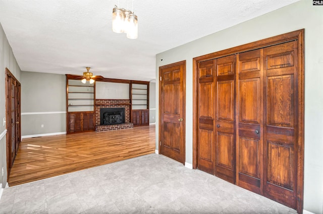 unfurnished living room with a textured ceiling, light wood-type flooring, a brick fireplace, and ceiling fan