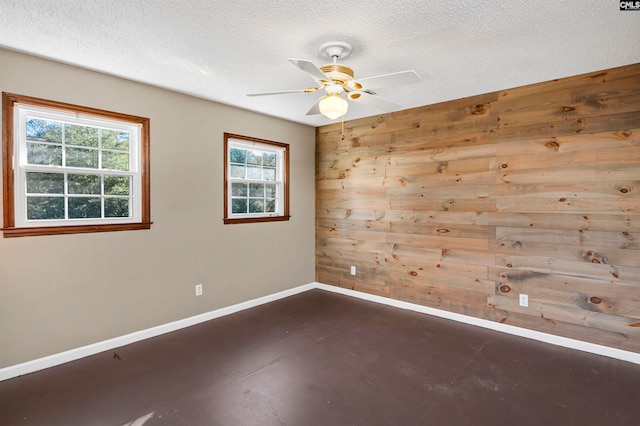 empty room featuring a healthy amount of sunlight, a textured ceiling, and wooden walls