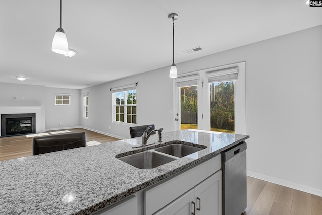 kitchen featuring sink, hanging light fixtures, stainless steel dishwasher, light wood-type flooring, and light stone counters