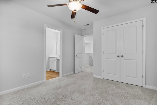 unfurnished bedroom with a closet, light colored carpet, ceiling fan, and ensuite bathroom