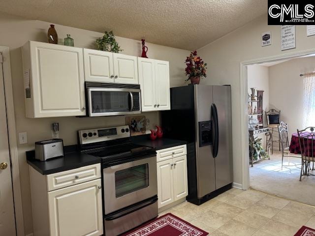 kitchen with light carpet, a textured ceiling, stainless steel appliances, white cabinetry, and lofted ceiling