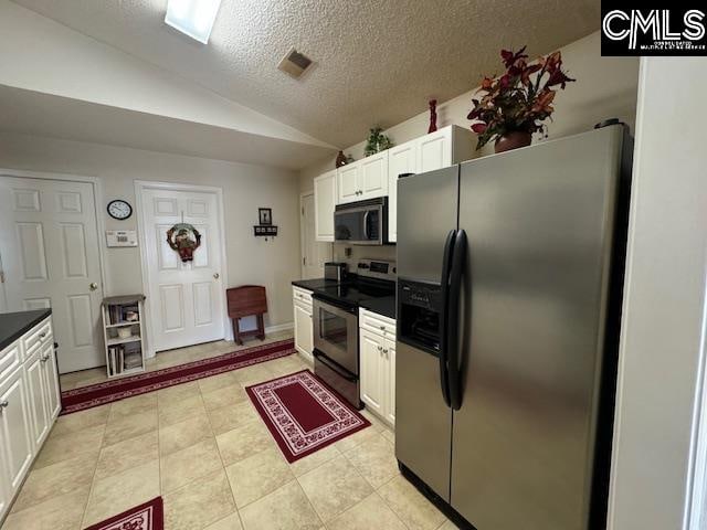 kitchen with white cabinetry, a textured ceiling, lofted ceiling, light tile patterned floors, and appliances with stainless steel finishes