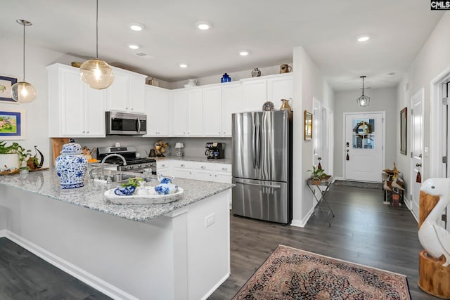 kitchen with dark wood-type flooring, stainless steel appliances, kitchen peninsula, decorative light fixtures, and white cabinets