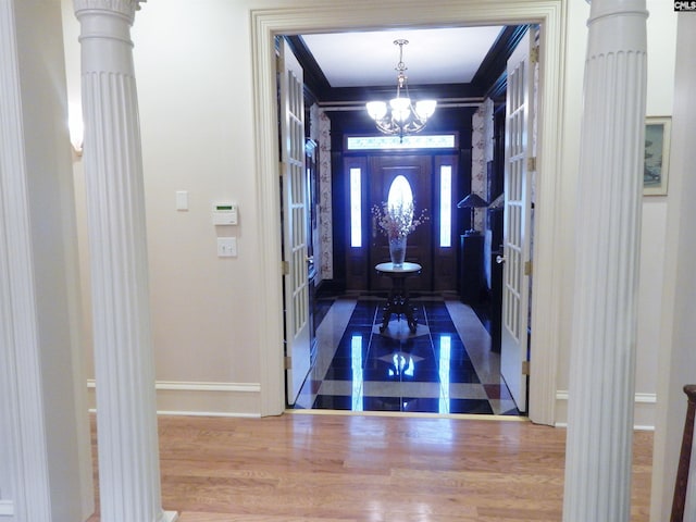 foyer entrance featuring decorative columns, ornamental molding, wood-type flooring, and a notable chandelier