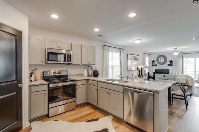 kitchen with kitchen peninsula, light stone countertops, stainless steel appliances, sink, and light hardwood / wood-style flooring