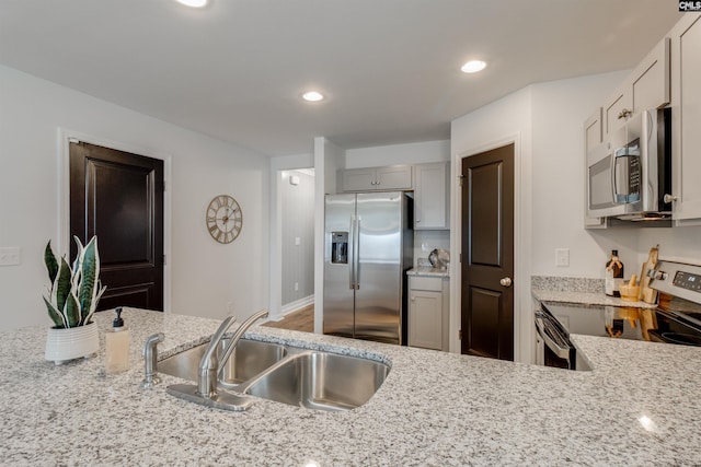 kitchen with gray cabinets, sink, light stone countertops, and stainless steel appliances