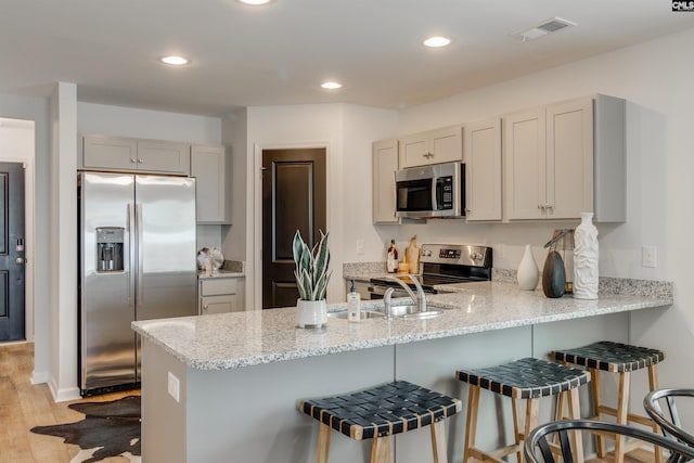 kitchen with a kitchen breakfast bar, kitchen peninsula, light hardwood / wood-style flooring, and stainless steel appliances