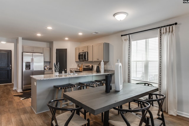 kitchen with gray cabinetry, sink, dark hardwood / wood-style floors, appliances with stainless steel finishes, and light stone counters