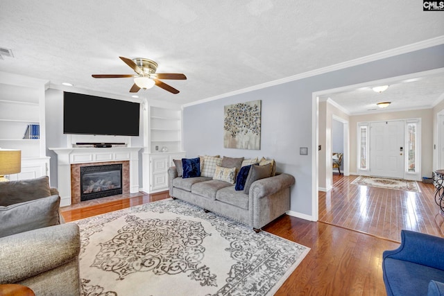 living room with crown molding, hardwood / wood-style flooring, ceiling fan, built in features, and a textured ceiling