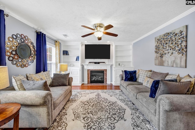 living room featuring wood-type flooring, a textured ceiling, crown molding, and a tiled fireplace