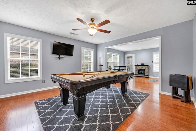 rec room featuring ceiling fan, a stone fireplace, wood-type flooring, a textured ceiling, and pool table