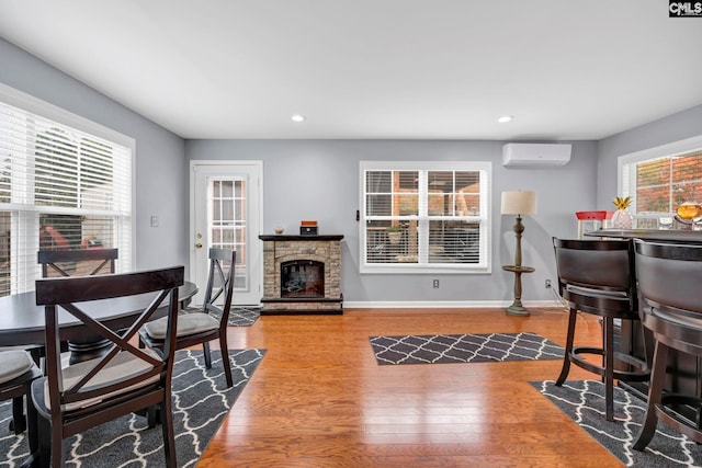 dining area featuring an AC wall unit, a stone fireplace, a healthy amount of sunlight, and hardwood / wood-style flooring