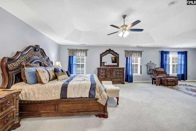 bedroom featuring a raised ceiling, ceiling fan, and light colored carpet