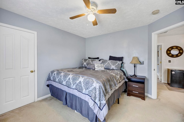 bedroom with ceiling fan, light colored carpet, and a textured ceiling