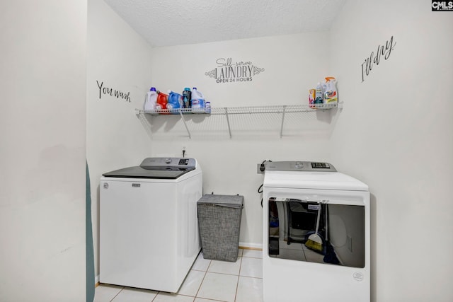 washroom with washing machine and clothes dryer, light tile patterned flooring, and a textured ceiling