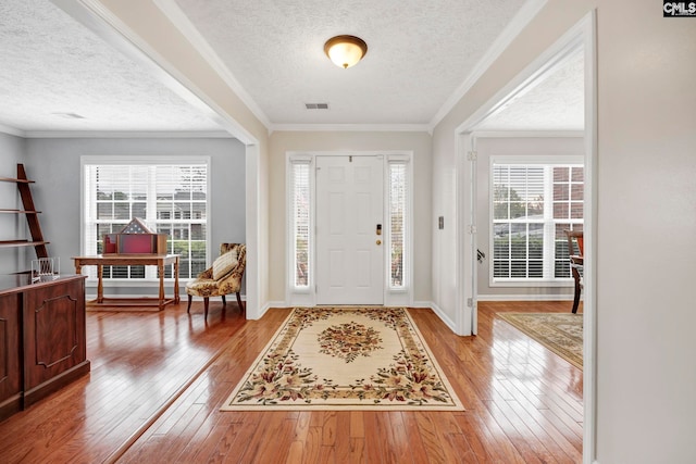 foyer entrance with light hardwood / wood-style floors, crown molding, and a textured ceiling