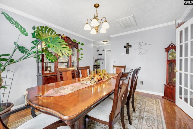 dining room featuring hardwood / wood-style flooring, a notable chandelier, crown molding, and a textured ceiling