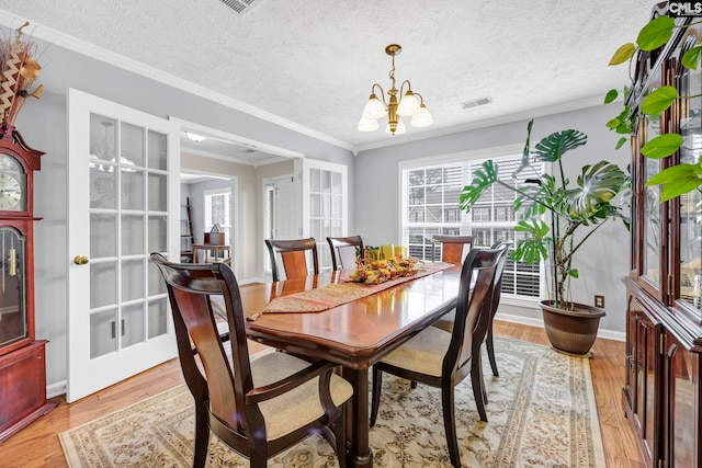 dining space featuring a textured ceiling, ornamental molding, a notable chandelier, and light wood-type flooring