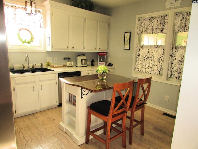 kitchen with stainless steel dishwasher, sink, white cabinets, light hardwood / wood-style floors, and hanging light fixtures