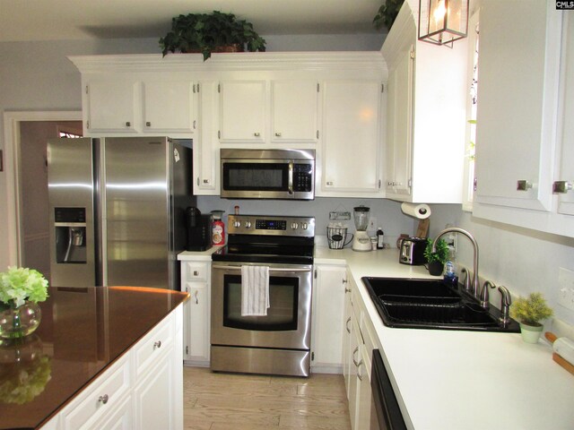 kitchen with pendant lighting, sink, light wood-type flooring, white cabinetry, and stainless steel appliances