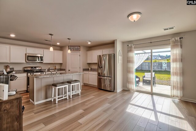 kitchen featuring a kitchen island with sink, white cabinets, hanging light fixtures, light hardwood / wood-style flooring, and stainless steel appliances