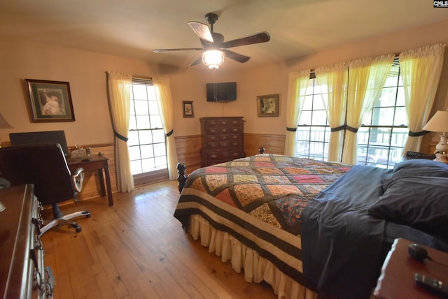 bedroom with ceiling fan, light hardwood / wood-style flooring, and wooden walls