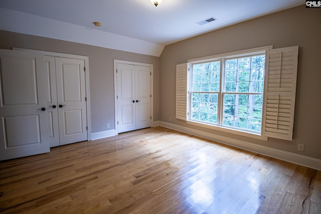 unfurnished bedroom with multiple closets, light hardwood / wood-style floors, and vaulted ceiling