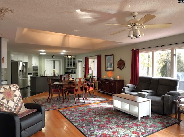 living room featuring a tray ceiling, ceiling fan, light hardwood / wood-style floors, and a textured ceiling