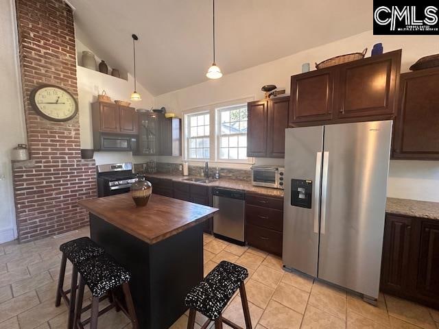 kitchen featuring appliances with stainless steel finishes, brick wall, sink, a kitchen island, and hanging light fixtures