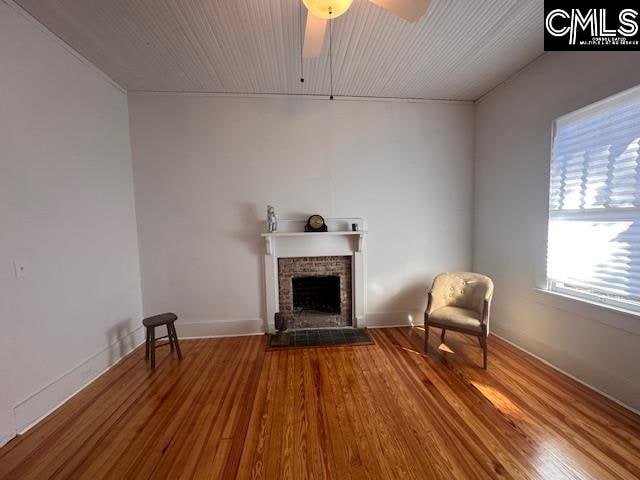 unfurnished room with hardwood / wood-style flooring, a brick fireplace, and ceiling fan