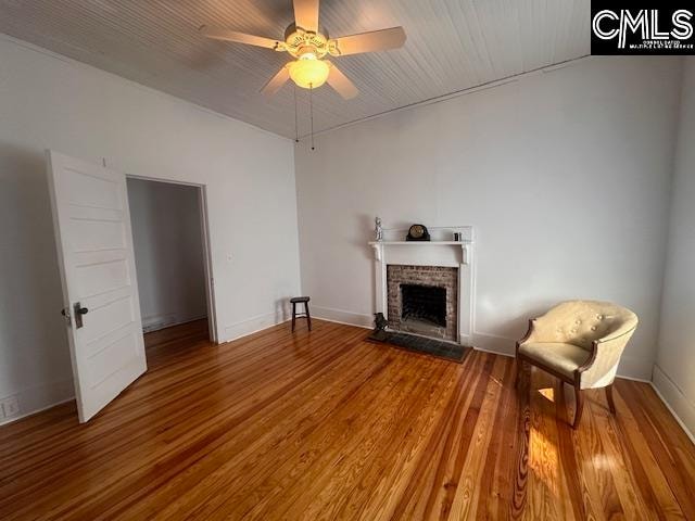 unfurnished room with ceiling fan, wood-type flooring, and a brick fireplace