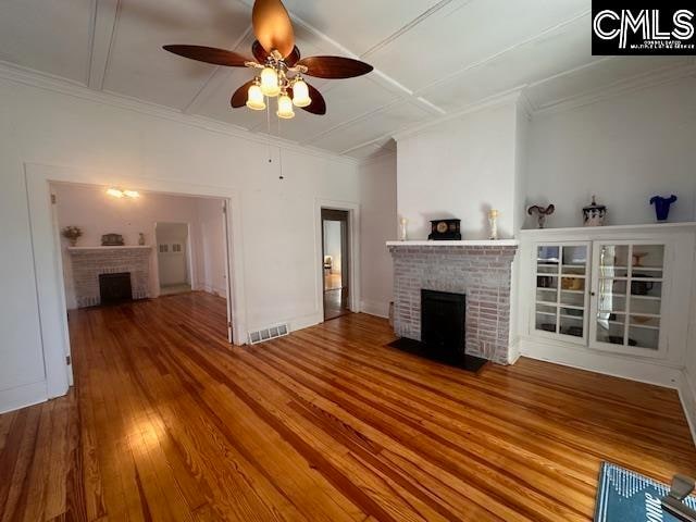 unfurnished living room with hardwood / wood-style flooring, ceiling fan, ornamental molding, and a brick fireplace