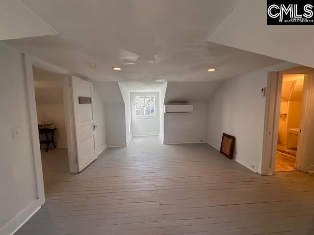 bonus room with a wall mounted AC, lofted ceiling, and light wood-type flooring