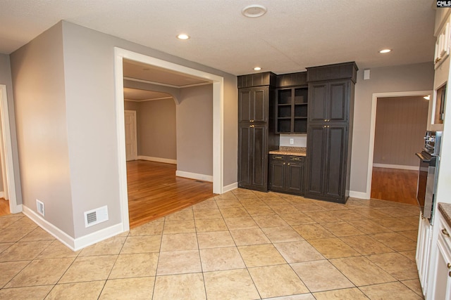 kitchen with dark brown cabinetry, oven, a textured ceiling, and light wood-type flooring